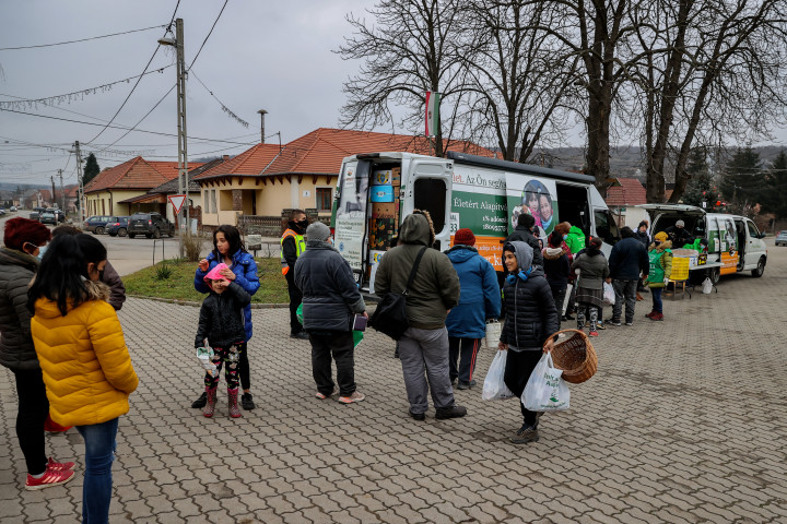 Emberek sétálnak el az osztáson kapott csomagokkal Szomolyán – Fotó: Huszti István / Telex