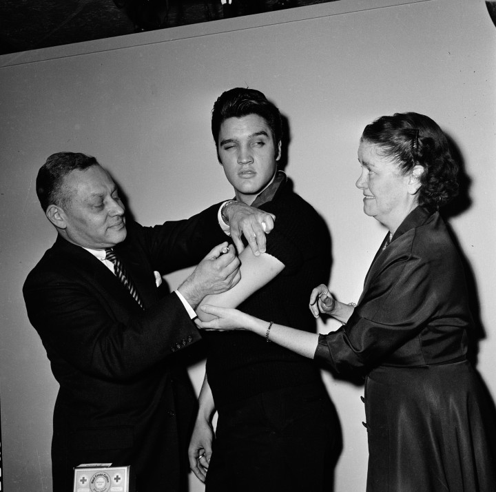 Az Ed Sullivan Show színfalai mögött Elvis Presley megkapja a gyerekbénulás elleni oltást. Jobbra New York városának egészségügyi biztosa, Leona Baumgartner, balra az ő asszisztense, Harold Fuerst – Fotó: CBS Photo Archive / Getty Images