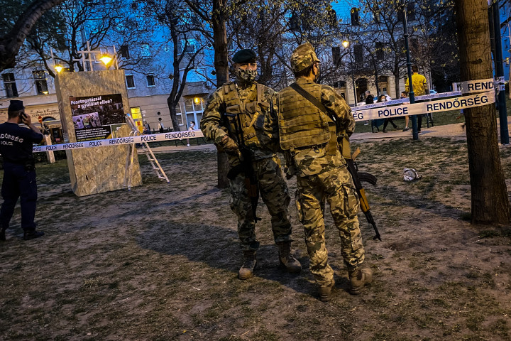 A már körbedeszkázott és -kordonozott szoborra vigyázó fegyveres katonák a Ferenc téren április elsején este. Fotó: Huszti István / Telex