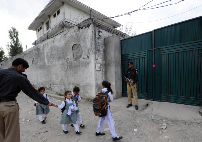 Pakisztáni iskolásokkal fog kezet egy rendőr Abbotábád városában, Oszama bin Laden és családja utolsó tartózkodási helyszíne előtt 2011-ben – Fotó: AAMIR QURESHI / AFP