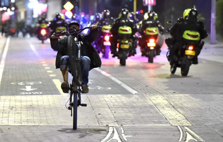 Egy férfi biciklizik Bogotában, miközben rendőrmotorosok tartanak a rendőri brutalitás elleni tüntetést felszámolni 2020 szeptemberében – Fotó: Raul Arboleda / AFP
