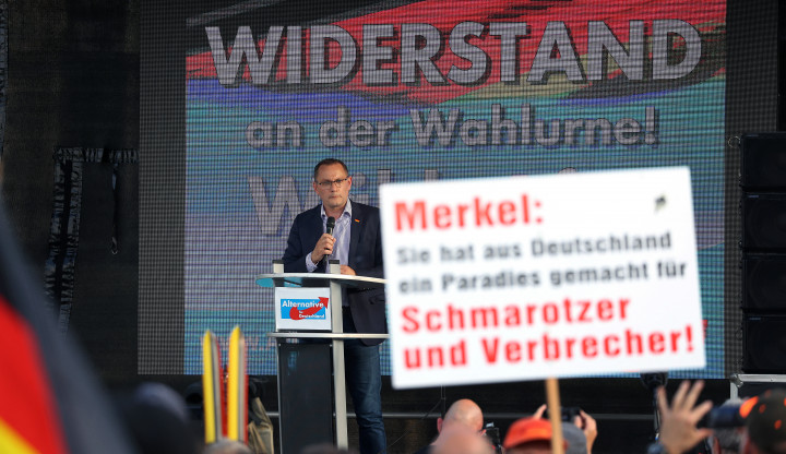 A kivetítőn: „Ellenállás az urnáknál!”, a táblán: „Merkel: Németországból megcsinálta az élősködők és bűnözők paradicsomát!” – Fotó: Ronny Hartmann / dpa Picture-Alliance via AFP