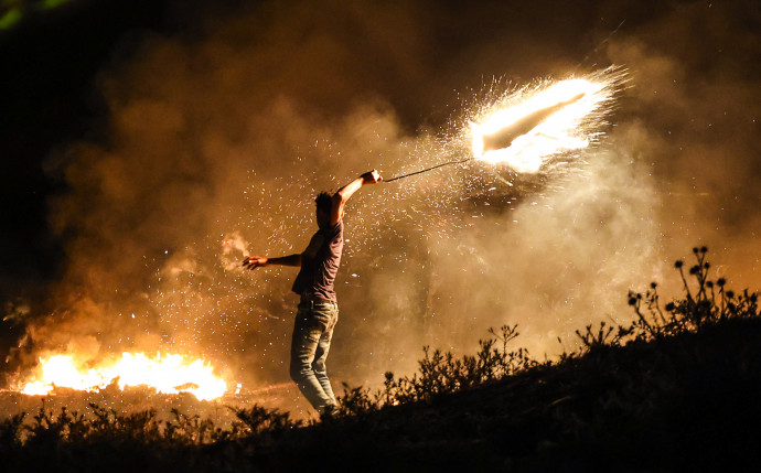 Egy palesztin tüntető égő lövedéket lendít a rendfenntartók felé egy tüntetésen Gáza keleti részén – Fotó: Mahmud Hams / AFP