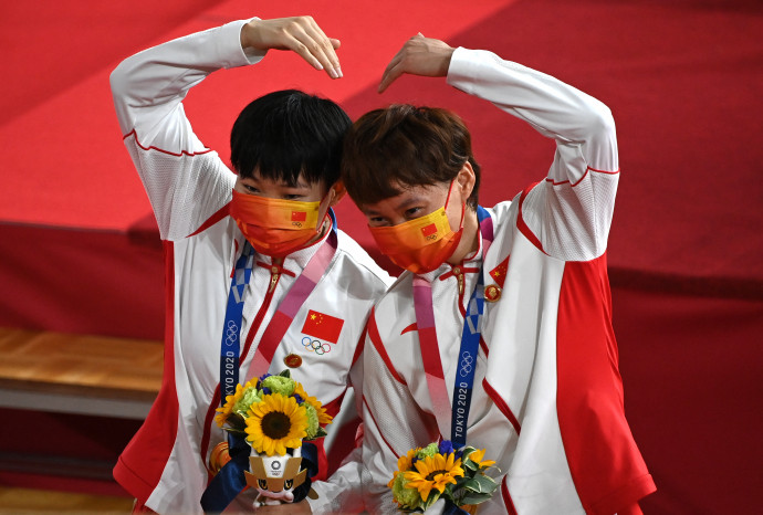 Pao San-csü és Csung Tien-si, a női csapatsprint győztes kínai párosa a díjátadó után, a Mao-kitűzők a melegítőn lévő kínai zászló mellett. Fotó: Greg Baker / AFP