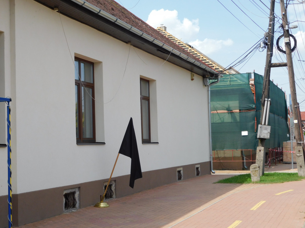 A bezenyei önkormányzat épületét felújítják, így a szomszédos művelődési háznál áll a helyi áldozatokra emlékeztető fekete zászló – Fotó: Cséfalvay Attila / Telex