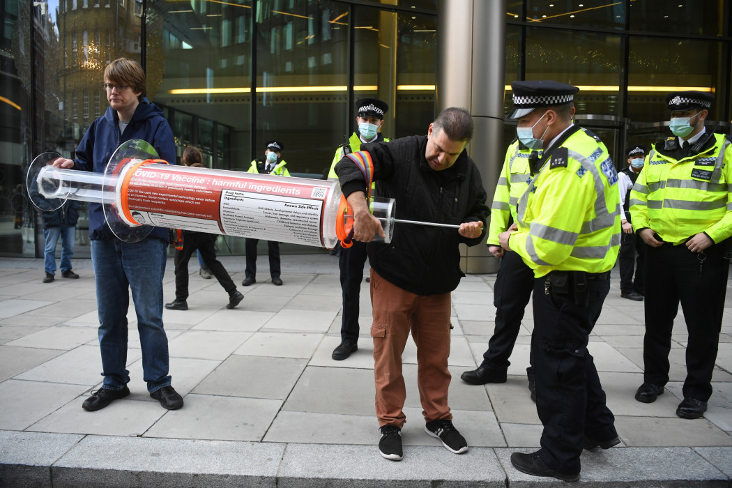 Óriási injekciós fecskendőt fognak tüntetők, akik az új koronavírus elleni oltások ellen tiltakoznak a Bill és Melinda Gates Alapítvány londoni épülete előtt 2021. november 24-én – Fotó: Neil Hall / EPA / MTI
