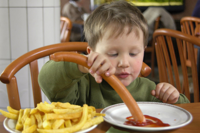 Egy fiú virslit eszik ketchuppal és sültkrumplival egy németországi gyorsétteremben – Fotó: Schöning / ullstein bild / Getty Images