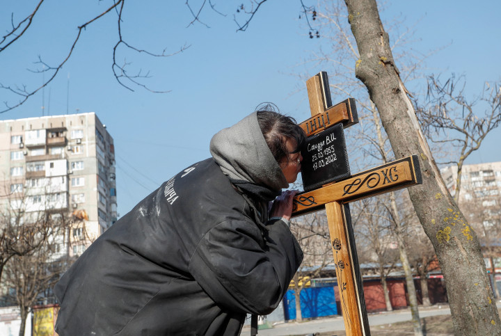 Egy asszony megcsókolja egy mariupoli lakótelepen eltemetett hozzátartozójának fejfáját március 23-án – Fotó: Alexander Ermochenko / Reuters
