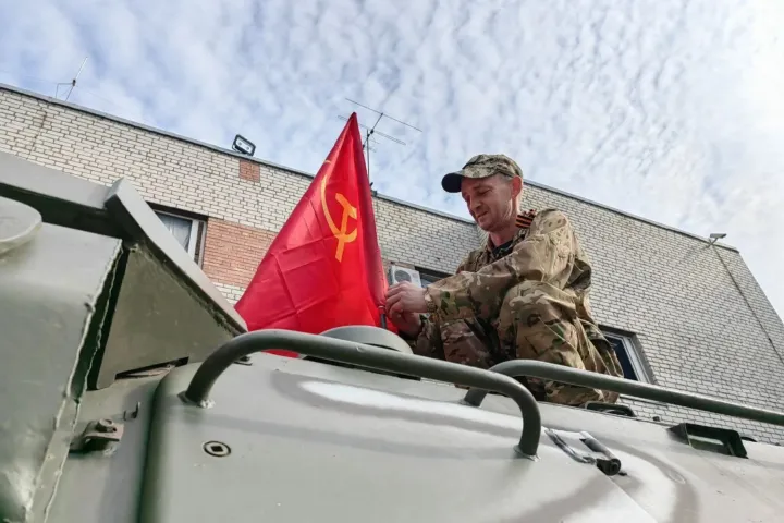 Egy férfi szovjet zászlót igazít egy páncélozott járművön a győzelem napján, Ukrajnában, a részben oroszok által ellenőrzött Harkiv régióban – Fotó: Sputnik / AFP