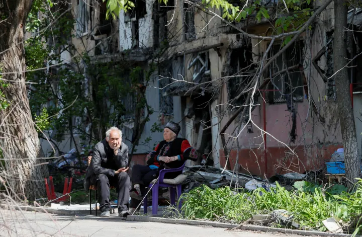 Megrongálódott épület előtt ülnek helyiek Mariupolban május 20-án – Fotó: Alexander Ermochenko / Reuters