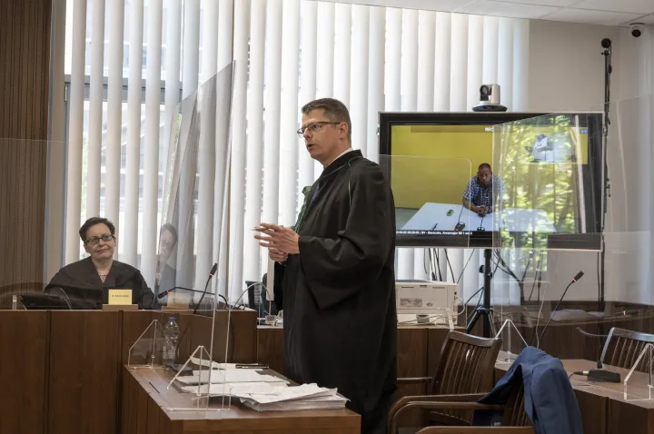 Enzsöl Péter ügyvéd, a háttérben a képernyőn H. Zoltán vádlott hallgatja – Fotó: Melegh Noémi Napsugár / Telex