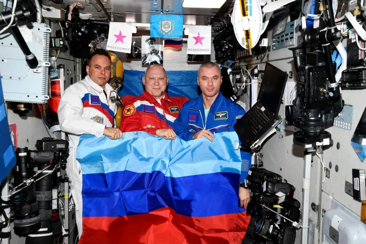 Oleg Artyemjev, Denisz Matvejev és Szergej Korszakov orosz űrhajósok pózolnak a Luhanszki Népköztársaság zászlajával a Nemzetközi Űrállomáson 2022. július 4-én – Fotó: Roszkoszmosz / Reuters