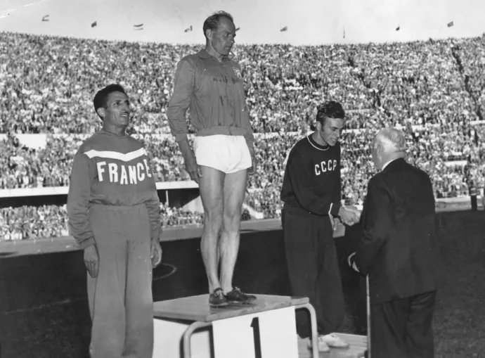 Emil Zátopek átveszi az 1952-es helsinki olimpiai aranyérmét, miután megnyerte a 10&#8239;000 méteres futást. A francia Alain Mimoun lett a második, a szovjet Alekszandr Anufrijev a harmadik a versenyen – Fotó: Central Press / Getty Images