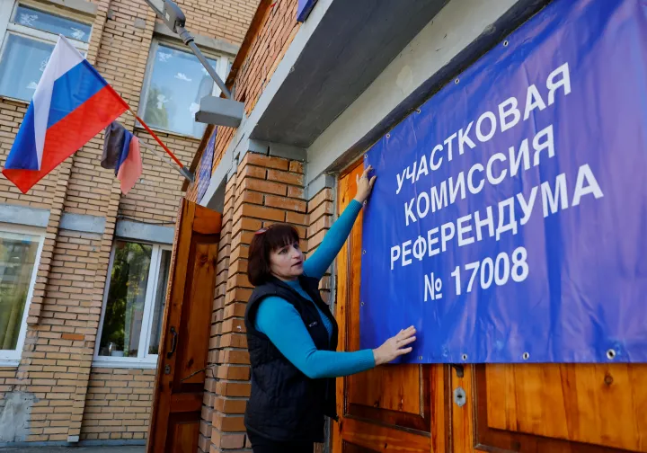 A helyi választási bizottság egyik tagja egy szavazóhelyiség ajtajára egy transzparenst akaszt egy szavazóhelyiség ajtajára a népszavazás előtt 2022. szeptember 22-én – Fotó: Alexander Ermochenko / Reuters