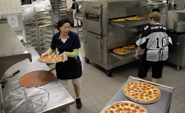 Szakácsok pizzát készítenek ebédre az Everglades középiskolában 2011. november 18-án a floridai Miramarban, miután a kongresszus elfogadta a törvényt, miszerint a pizzán lévő paradicsomszósz mennyisége fedezi a napi zöldségbevitelt – Fotó: Joe Raedle / Getty Images