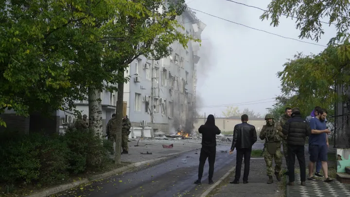 Katonák és helyiek várják a tűzoltókat, miután felrobbant egy autóba rejtett bomba az egyik helyi televízió épülete előtt Melitopolban október 25-én – Fotó: Anadolu Agency / AFP