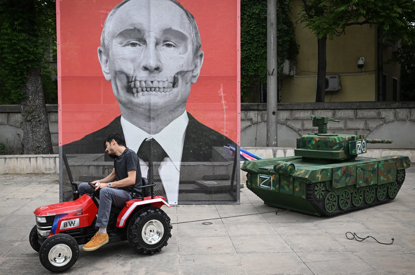 Az Aresel roma civil szervezet egyik tagja odahúz egy orosz tank makettet Vlagyimir Putyin orosz elnök portréja elé, 2022. május 16-án. Több roma aktivista is tiltakozott a bukaresti orosz nagykövetség előtt, miután a sajtó egy részében hamisan azt állították, hogy az ukrán romák elloptak egy orosz tankot – Fotó: Daniel Mihailescu / AFP