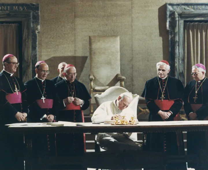 János Pál pápa aláírja az új római katolikus egyházi törvénykönyvet 1983. január 25-én, mögötte jobbra Ratzinger bíboros – Fotó: Bettmann / AFP