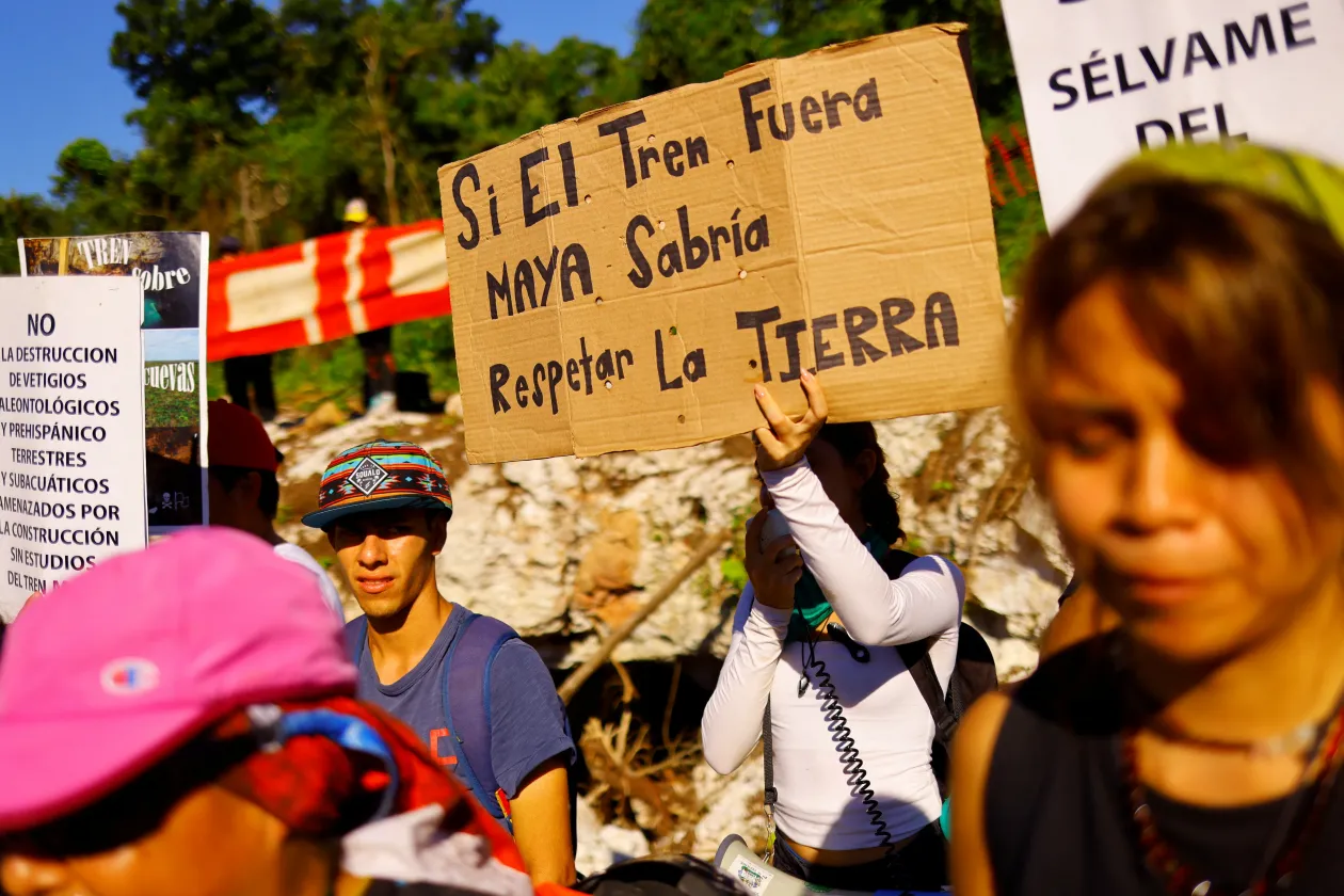 Juan Maxcanúban figyeli a vasútvonal építését, amely elmondása szerint lerombolta otthona egy részét. / Egy tüntető „Ha a vonat maja lenne, tudná, hogyan kell tisztelni a földet” feliratú táblát tart, miközben aktivisták és helyiek a új vasútvonal környezeti hatásai ellen tiltakoznak a Yorogana-barlang előtt Playa del Carmenben – Fotó: Jose Luis Gonzalez / Reuters