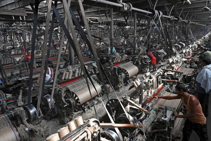In this picture taken on March 19, 2021, labourers work at a private jute mill in Jagatdal. – From the boutiques of Christian Dior to royal wedding favours, jute is growing in popularity worldwide as demand for alternatives to plastic soars, with experts predicting the bag industry alone will be worth more than 3 billion USD by 2024. (Photo by Dibyangshu SARKAR / AFP) / TO GO WITH AFP STORY India-Environment-Textile-Jute by Abhaya SRIVASTAVA