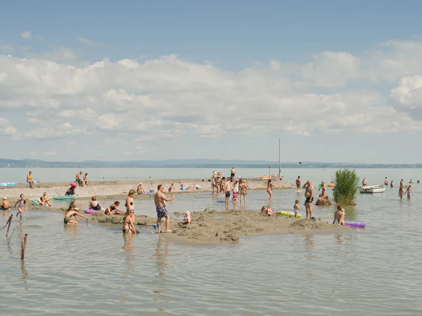 Fürdőzők az alacsony vízállású Balatonban a nyári kánikula idején. Siófok, Balaton, Veszprém megye Hőhullámok idején az emberek a városokból a vízpartok mellett hűsölnek. De a Balaton (Magyarország legnagyobb, 592km2 kiterjedésű természetes tava) vízszintje is folyamatosan csökkent. Májusban a tó átlagos vízszintje 105 cm körül volt. Augusztus végére 78 cm-re csökkent.