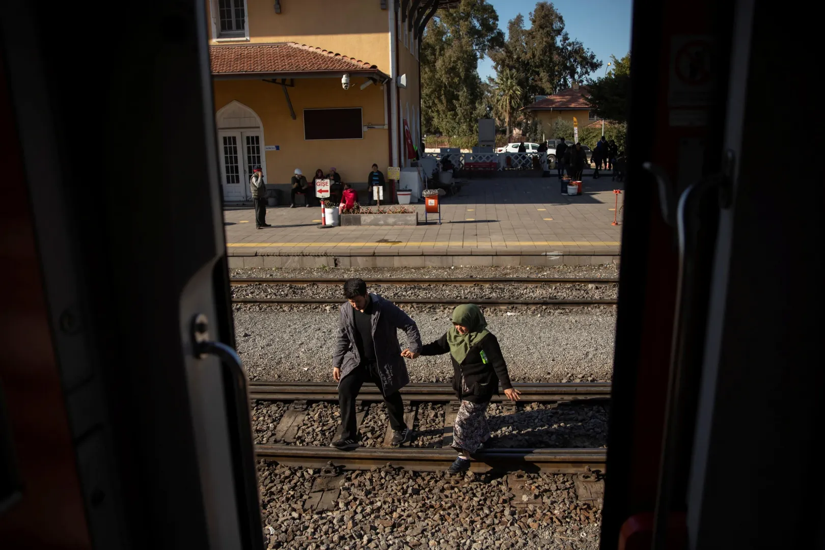 Egy férfi átsegít egy nőt a síneken az ıskenderuni vasútállomáson azokhoz a kocsikhoz, amelyeket most ideiglenes szállásként használnak – Fotó: Eloisa Lopez / Reuters