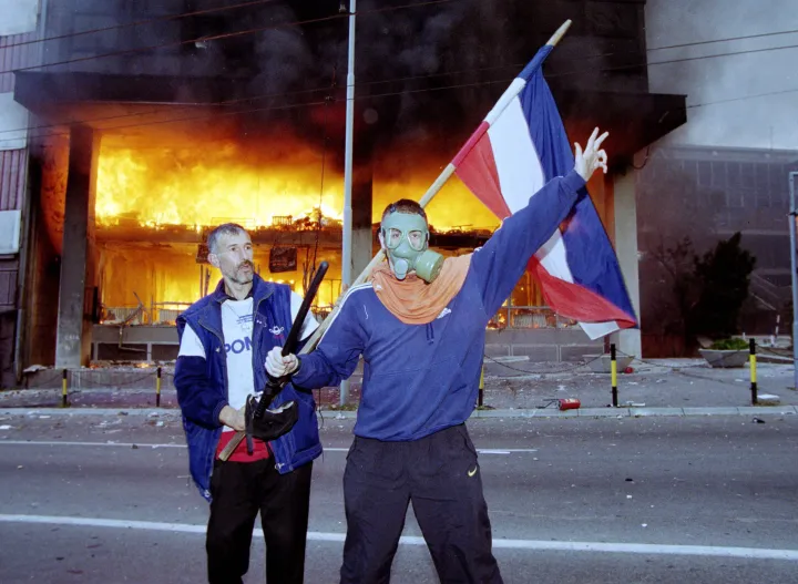 Tüntetők az állami televízió épülete előtt Belgrádban 2000. október 5-én, egyikük kezében a jugoszláv zászló, másikuk kezében egy gumibot – Fotó: Braca Nadezdic / Newsmakers via Getty Images