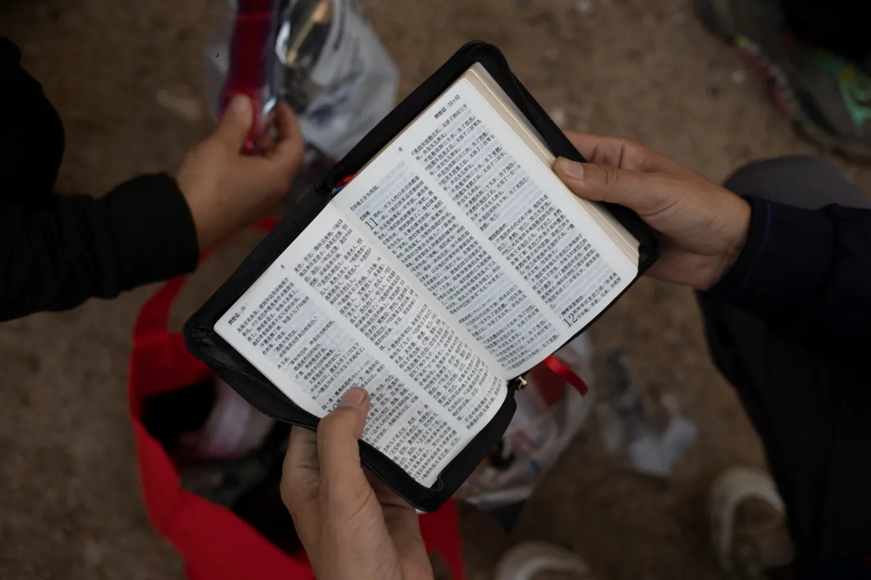 Egy Kínából érkező nagymama segít pelenkát cserélni egy három hónapos csecsemőn a határőrség egyik állomáshelyén. Jobbra egy férfi épp azt kéri a határőröktől, hogy hadd tartsa magánál a Bibliáját, ne kelljen leadnia a többi értékével együtt – Fotó: Reuters