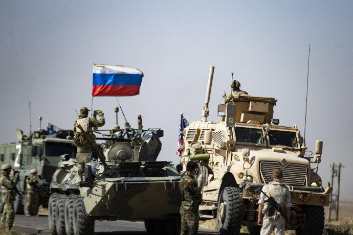 Soldiers of a Russian military convoy and their US counterparts exchange greetings as their patrol routes intersect in an oil field near Syria's al-Qahtaniyah town in the northeastern Hasakah province, close to the border with Turkey, on October 8, 2022. (Photo by Delil SOULEIMAN / AFP)