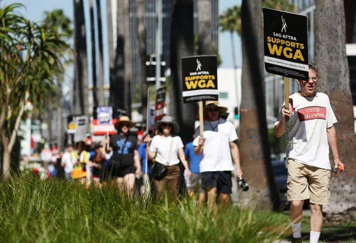 A SAG-AFTRA tagjai a sztrájkoló WGA dolgozókkal szolidaritást vállalva sztrájkolnak "A SAG-AFTRA támogatja a WGA-t" feliratú táblákkal a Netflix irodái előtt 2023. július 13-án – Fotó: Mario Tama / Getty Images / AFP