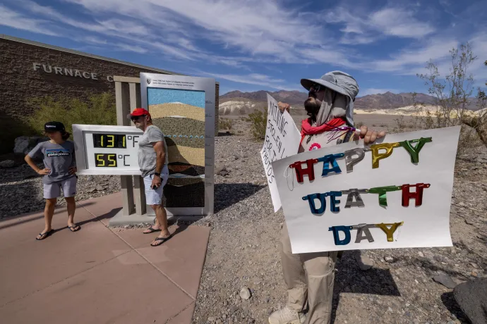 Turisták fotózkodnak a Furnace Creek-i hőmérővel 2023. július 16-án. A transzparensen olvasható felirat: „Boldog halálnapot!” – Fotó: David Mcnew / Getty Images / AFP