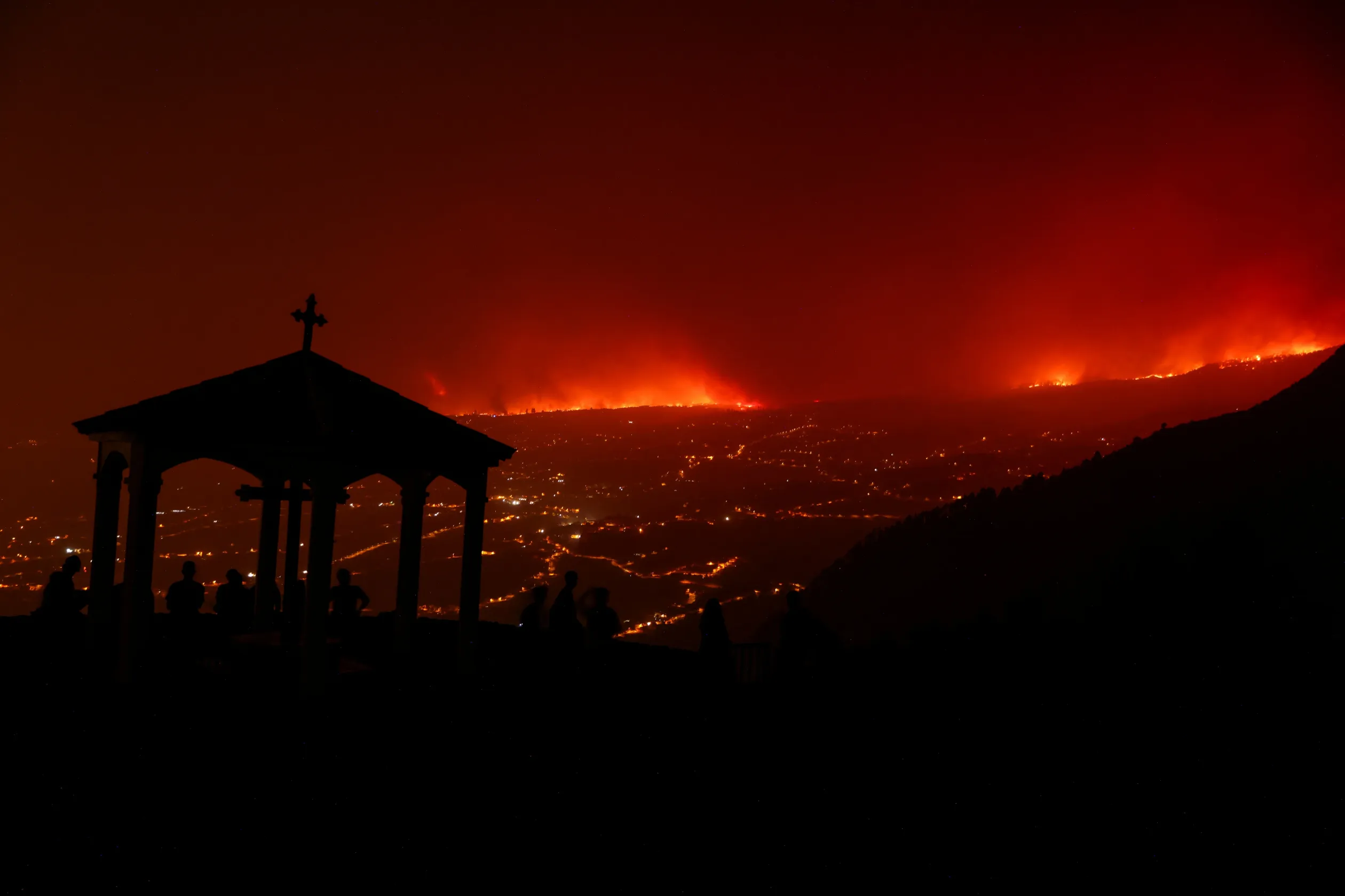 Erdőtüzek égnek a riasztás miatt elhagyott házak mögötti hegyekben Tenerifén, miközben a helyiek egy távoli dombról figyelik a katasztrófahelyzetet – Fotó: Nacho Doce / Reuters