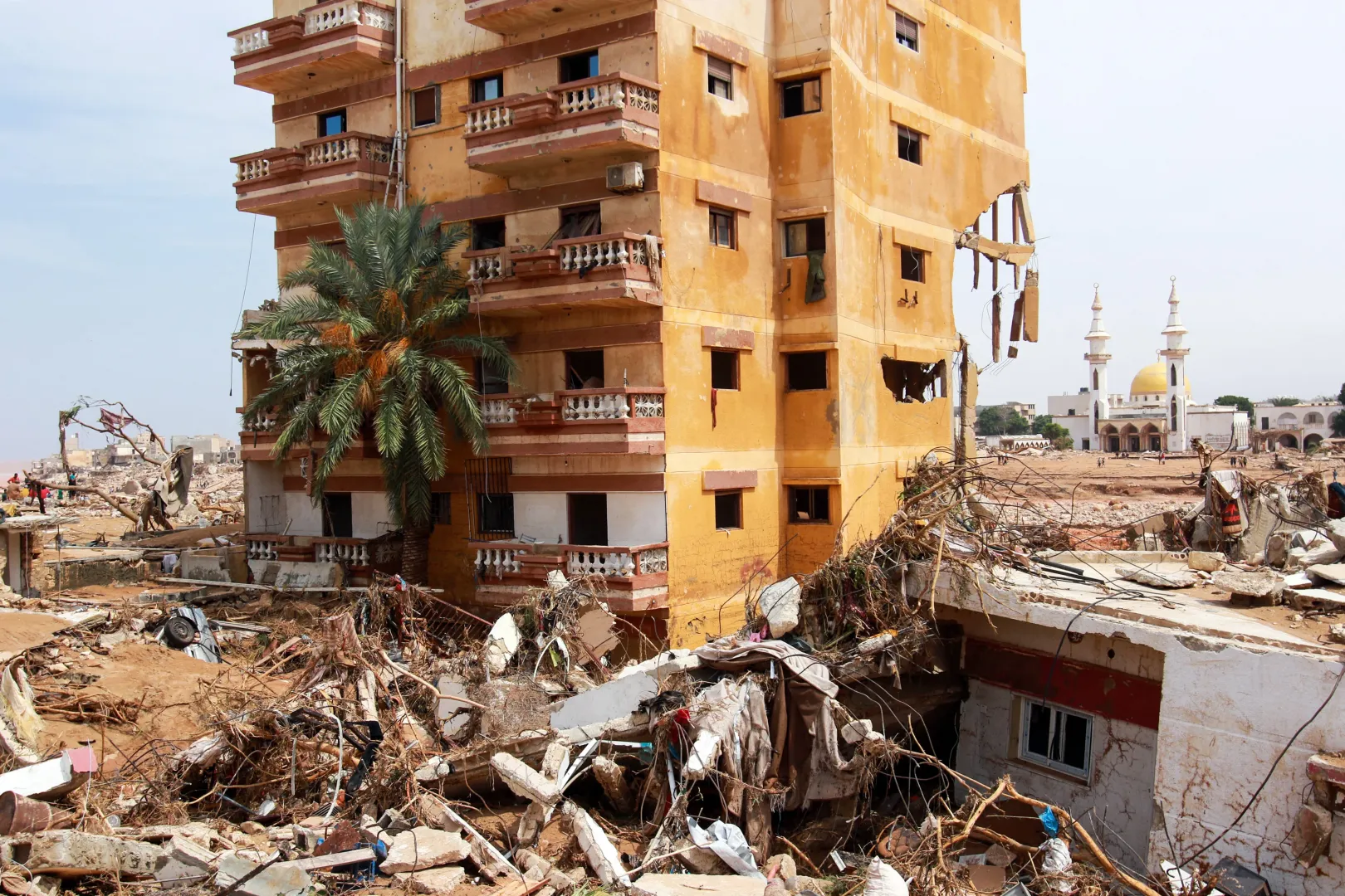 Pálmafa a ház előtt, mecset a háttérben, romok mindenhol Dernában 2023. szeptember 11-én – Fotó: AFP