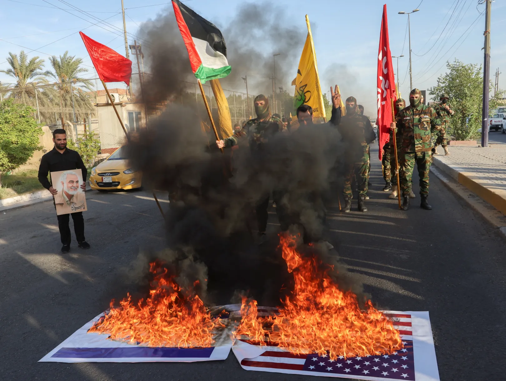 Amerikai és izraeli zászlók égnek, miközben a Harakat Hezbollah al Nujaba tagjai a tűz mellett gyülekeznek a gázai palesztinokkal való szolidaritási tüntetésen, az iraki Bagdadban – Fotó: Ahmed Saad / Reuters