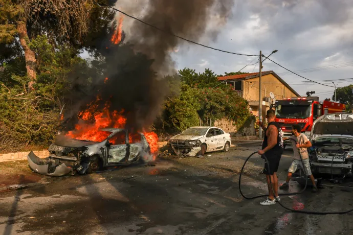 Emberek oltjanak egy a gázából érkező rakétatámadásban megsérült lángoló autót a dél-izraeli Askelón városában 2023. október 9-én – Fotó: Menahem Kahana / AFP