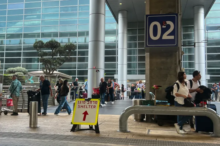 Utasok várakoznak az izraeli Ben Gurion nemzetközi repülőtéren, az előtérben egy óvóhely irányát mutató tábla – Fotó: Alexi J. Rosenfeld / Getty Images