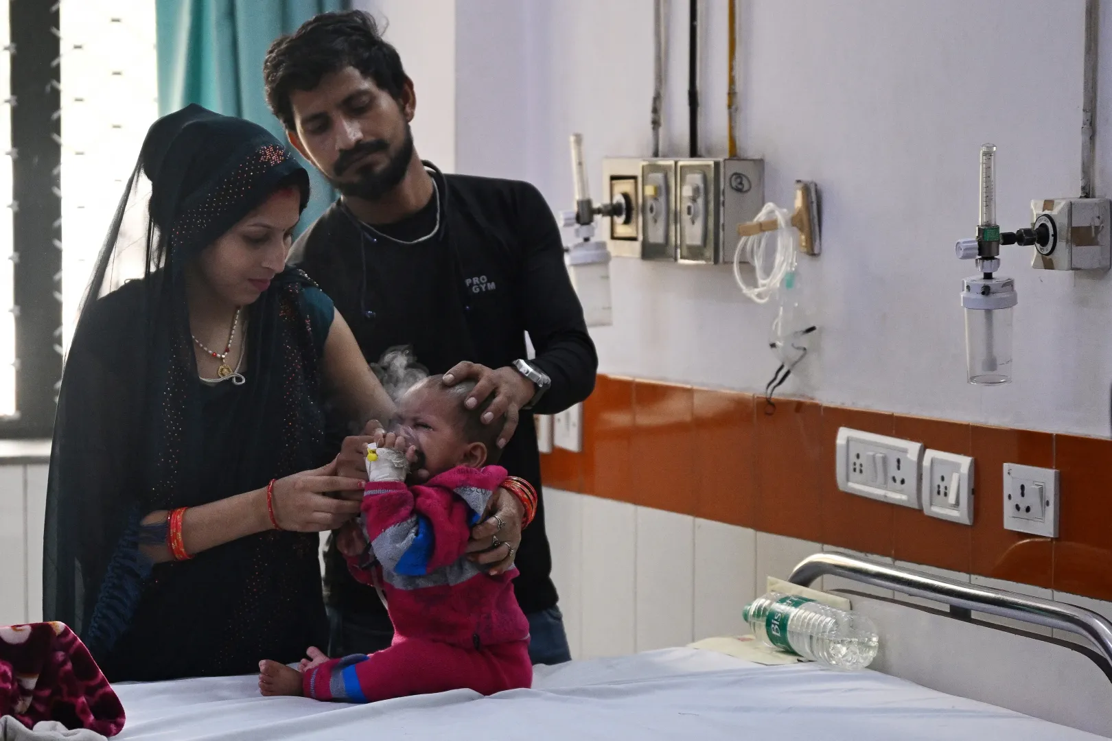 Szülők porlasztó segítségével segítik lélegezni gyermeküket a kormány által vezetett Chacha Nehru Bal Chikitsalaya gyermekkórház sürgősségi osztályán – Fotó: Arun Sankar / AFP