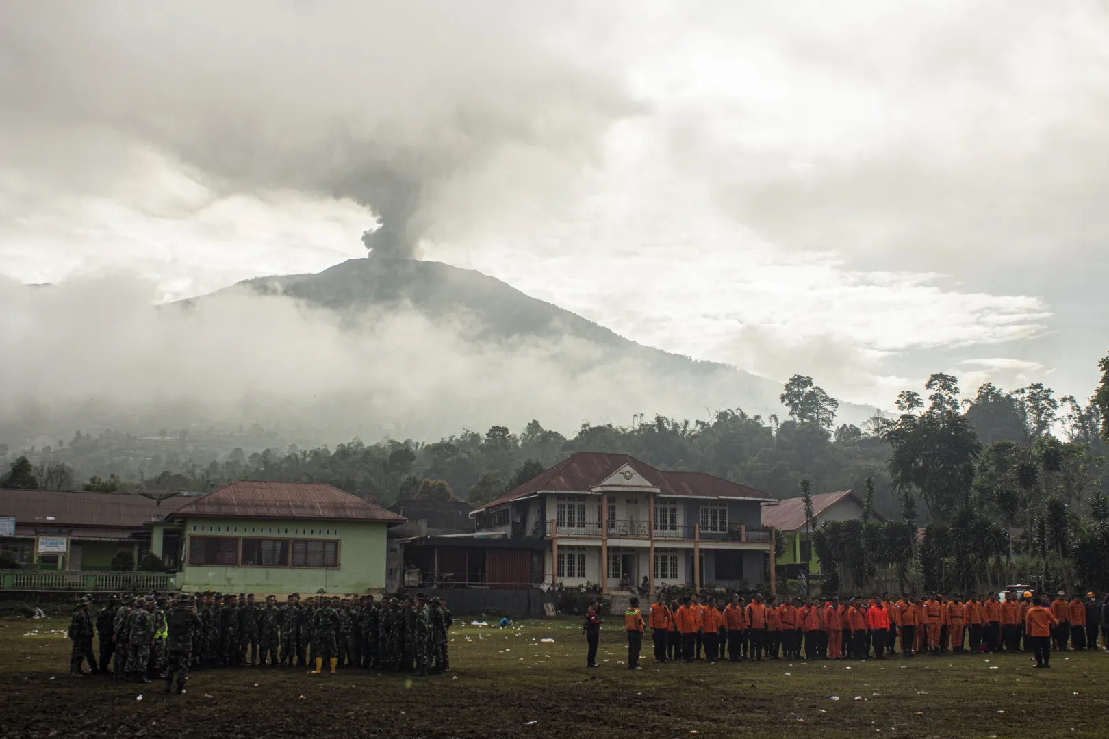 Egy indonéz kutató- és mentőcsapat tagjai létszámellenőrzést tartanak a mentés után, 2023. december 7-én, háttérben a füstölgő Marapi – Fotó: Adi Prima / AFP or