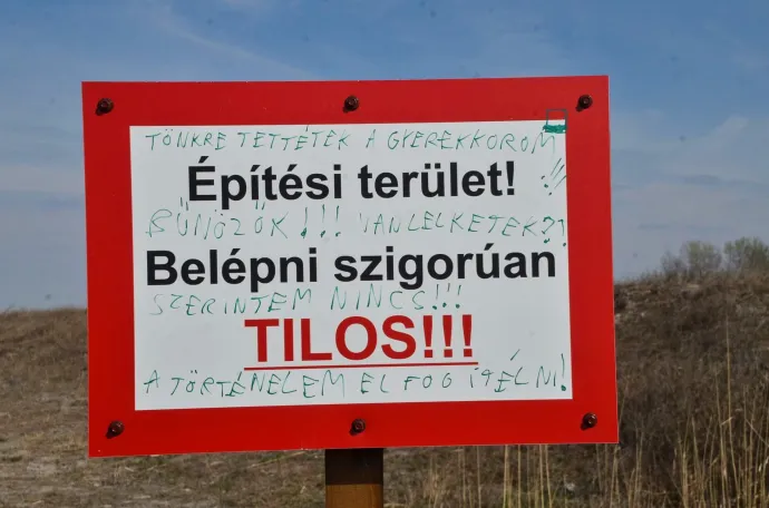 Kerítés az építési terület határán és egy üzenet az építkezés területét jelző táblán – Fotó: Nagy Márta / Telex