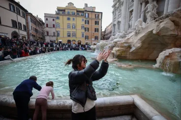 A tönk szélére került embereken segítenek a római Trevi-kutat érmékkel teledobáló turisták