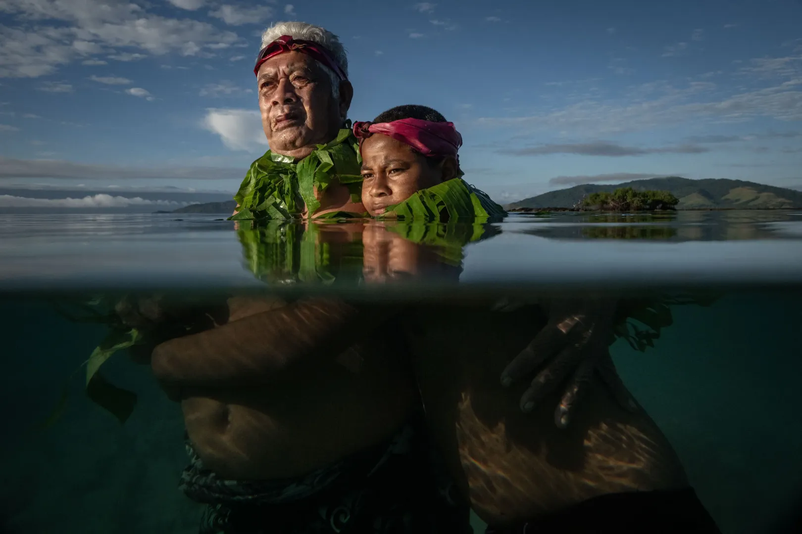 Lotomau Fiafia (72), a közösség idős tagja unokájával, Johnnal áll azon a ponton, ahol emlékei szerint gyerekkorában még partvonal húzódott. Salia-öböl, Kioa-sziget, Fidzsi-szigetek, 2023. augusztus 8. 