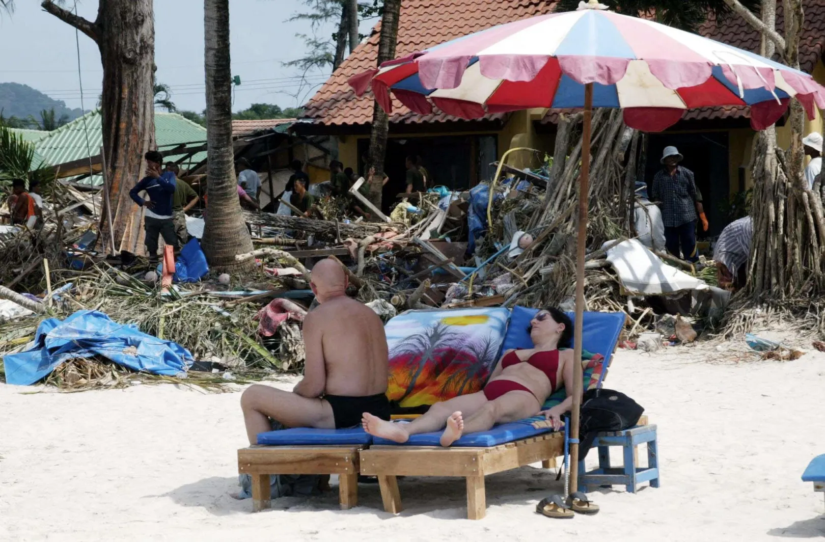 Turisták pihennek 2004. december 31-én a thaiföldi Patong Beachen, a háttérben a cunami törmelékét takarítják – Fotó: AFP