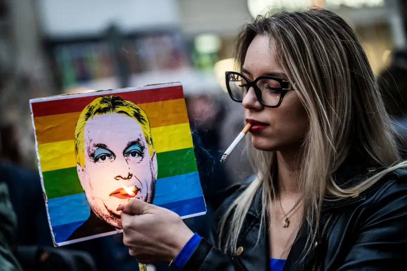 Szivárványos zászló hever a rendőrök előtt egy tüntetésen március 25-én, miután a magyar parlament elfogadta a Pride megtiltását célzó törvényt, korlátozva a gyülekezési jogot // Egy nő meggyújtja az Orbán Viktor magyar miniszterelnököt ábrázoló plakát cigarettáját – Fotó: Mónus Márton / Reuters