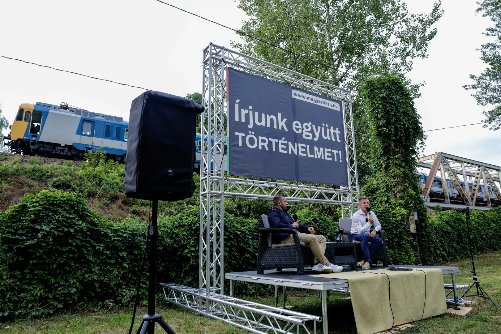 Személyvonat érkezik a tokaji hídról, miközben Magyar Tárkányi Zsolt Tisza-sajtóssal beszélget – Fotó: Huszti István / Telex