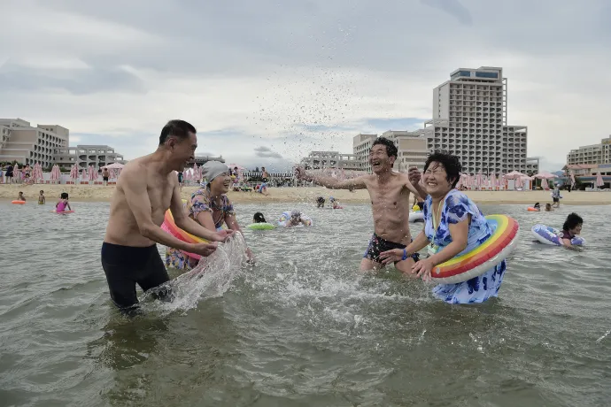 A propagandaképeken fürdőzők a strandon, alul Kim Dzsongun és lánya egy csúszdázó férfit tekintenek meg – Fotó: Kim Won Jin / AFP