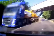 Videón, ahogy egy kamion tetején utazó markológép megakad egy felüljárón, és az útra zuhan