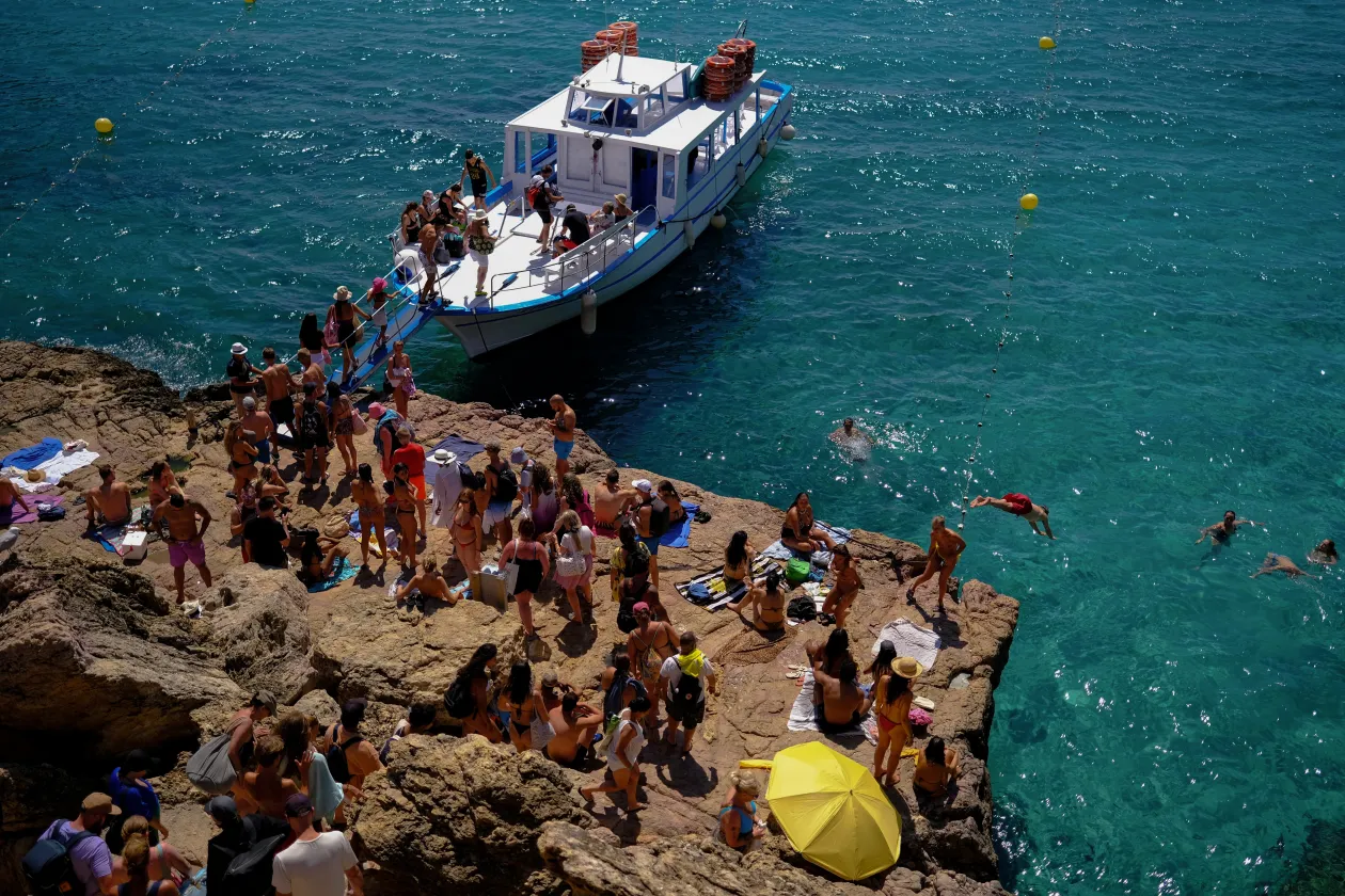 Turisták szállnak hajóra a Cala Saladeta strandon, Sant Antoni de Portmanyhoz közel / Egy turista tesz le egy üveg bort ugyanezen a strandon egy sziklára – Fotó: Nacho Doce / Reuters