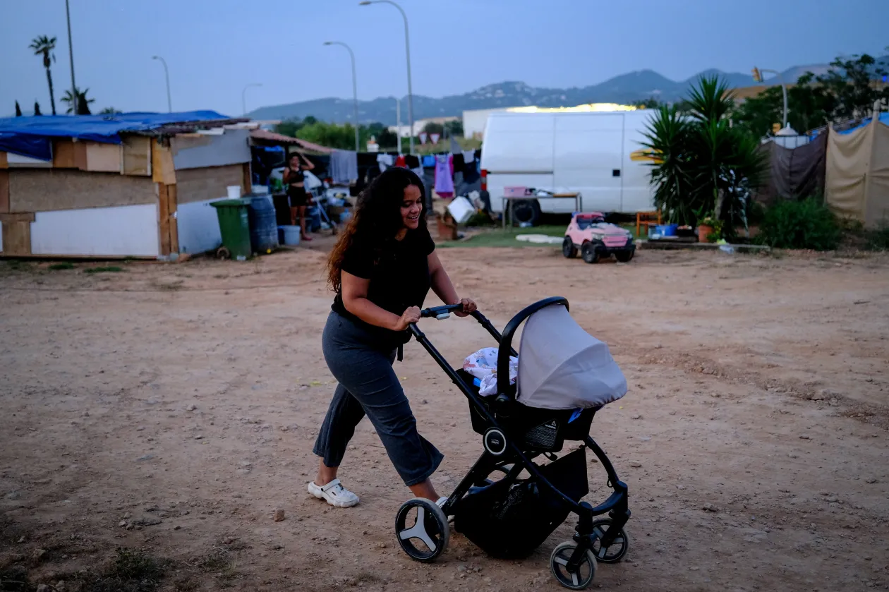 A 28 éves Rosario kisgyerekét tologatja babakocsiban a Can Rova 2 nevű telepen / Daisy, egy kolumbiai bevándorló elmosogat lakókocsija előtt – Fotó: Nacho Doce / Reuters