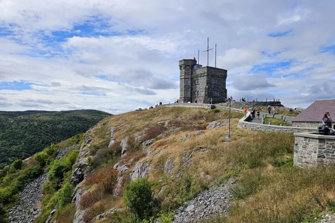 A Signal Hillre vezető East Coast Trail pallós szakasza, két, öbölre néző fafotelben pihenő kiránduló, a Signal Hill a Cabot-toronnyal – Fotó: Molnár Zoltán / Telex