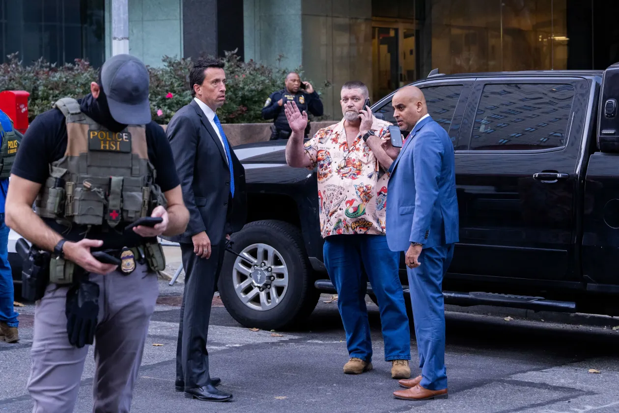 Állig felfegyverzett szövetségi ügynökök strázsálnak egy BearCat páncélozott szállítójármű mellett, az előtérben New York-i rendőrök; a jobboldali képen pedig a belbiztonsági minisztérium egyik bevetési parancsnoka, a posztjához képest igen laza szerelést viselő William Joyce int a fotósnak egy 2025. október 21-én végrehajtott New York-i akció során – Fotó: Adam Gray / Getty Images